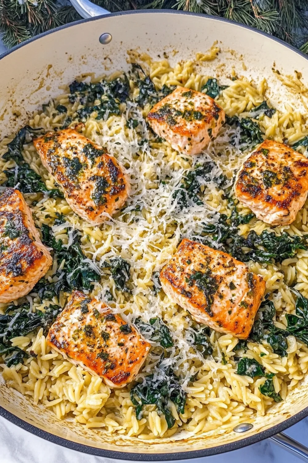 A one-pan dish featuring perfectly cooked salmon on top of lemon orzo pasta and sautéed kale, garnished with grated parmesan cheese.