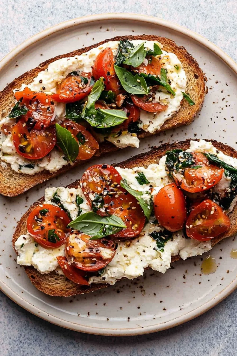 Two slices of toasted bread topped with creamy tuna salad, fresh cherry tomatoes, leafy herbs, and a sprinkle of seasonings.