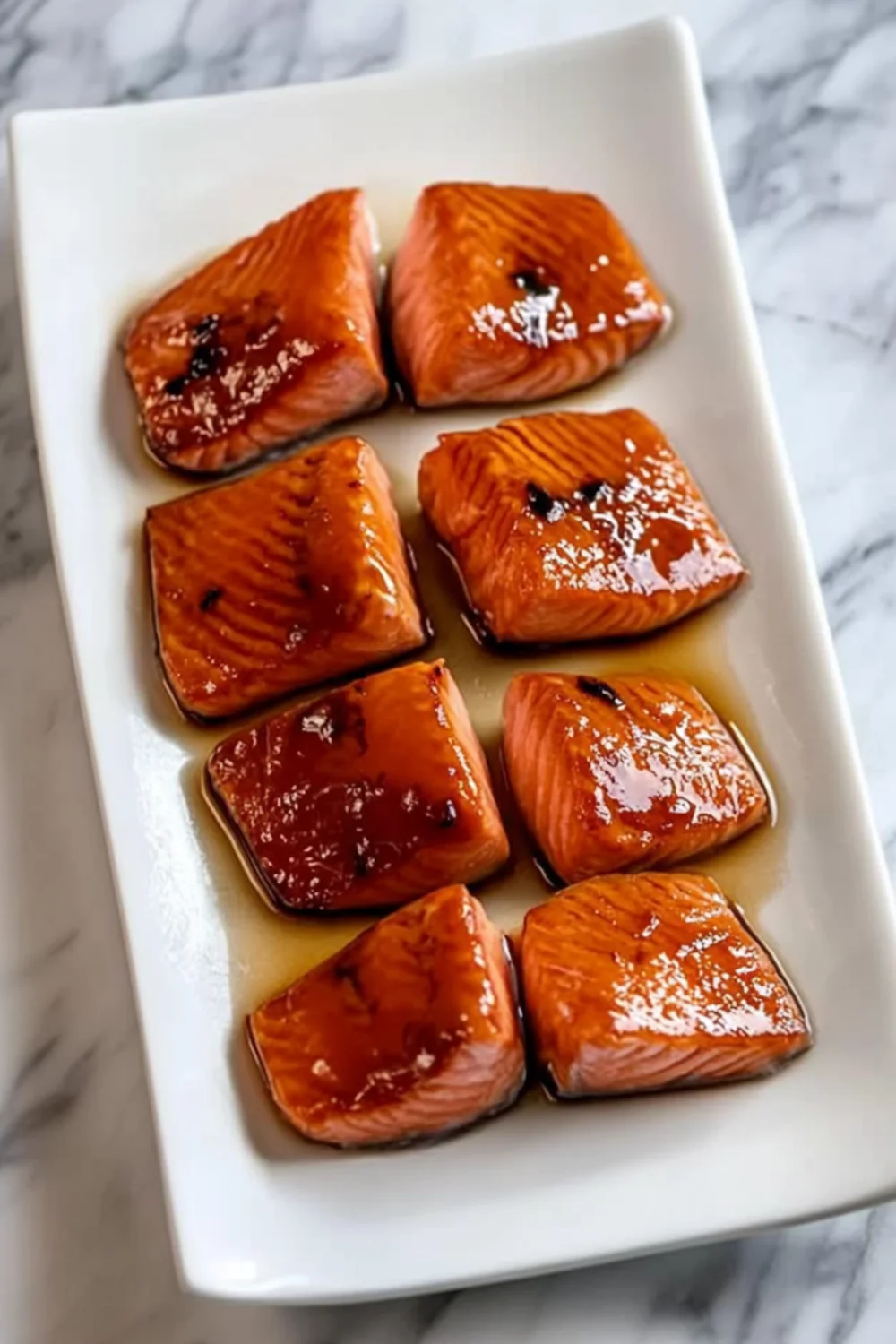 A close-up view of perfectly glazed brown sugar salmon fillets arranged on a white plate, with a shiny caramelized finish from the sweet glaze.